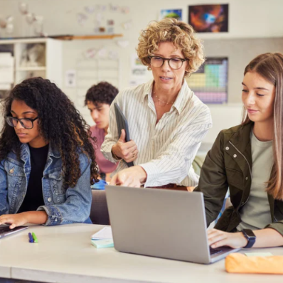 teacher helping students at a computer